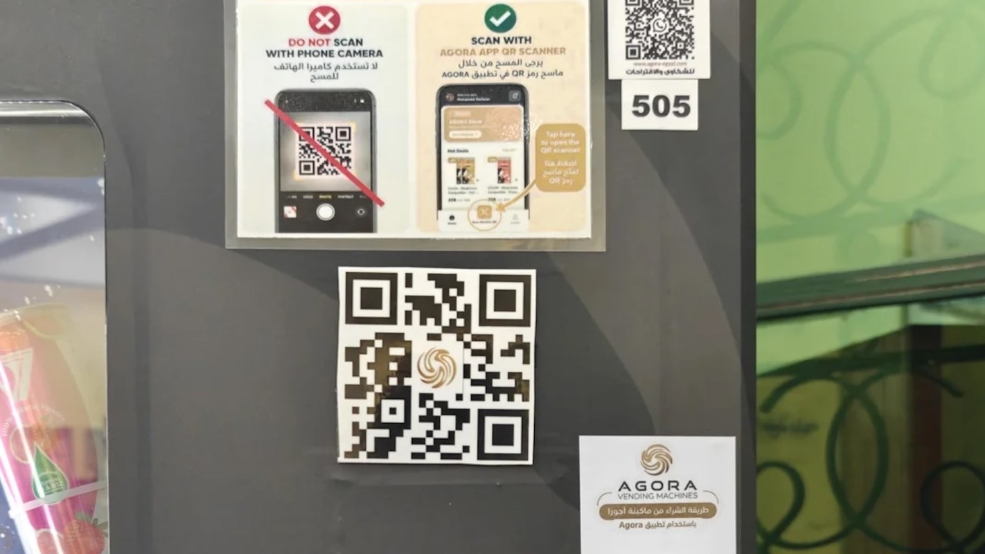 A sign on a vending machine displaying QR code instructions and the Agora vending machines logo.
