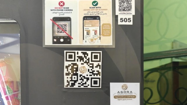 A sign on a vending machine displaying QR code instructions and the Agora vending machines logo.