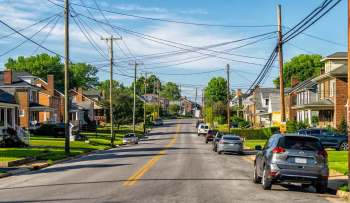 A neighborhood street lined with houses, utility poles, and parked cars.