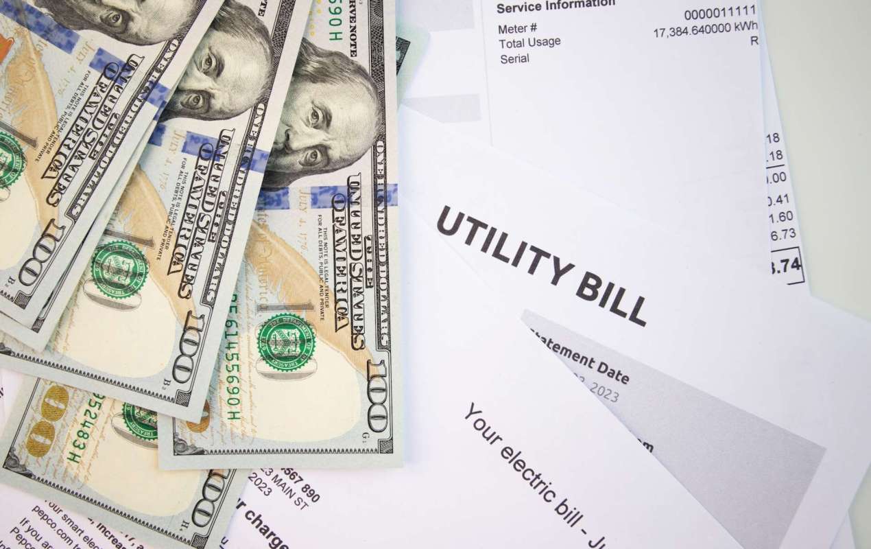 Several hundred-dollar bills are placed on top of various utility bills.
