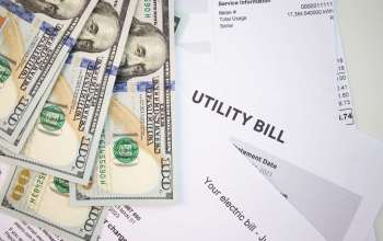 Several hundred-dollar bills are placed on top of various utility bills.