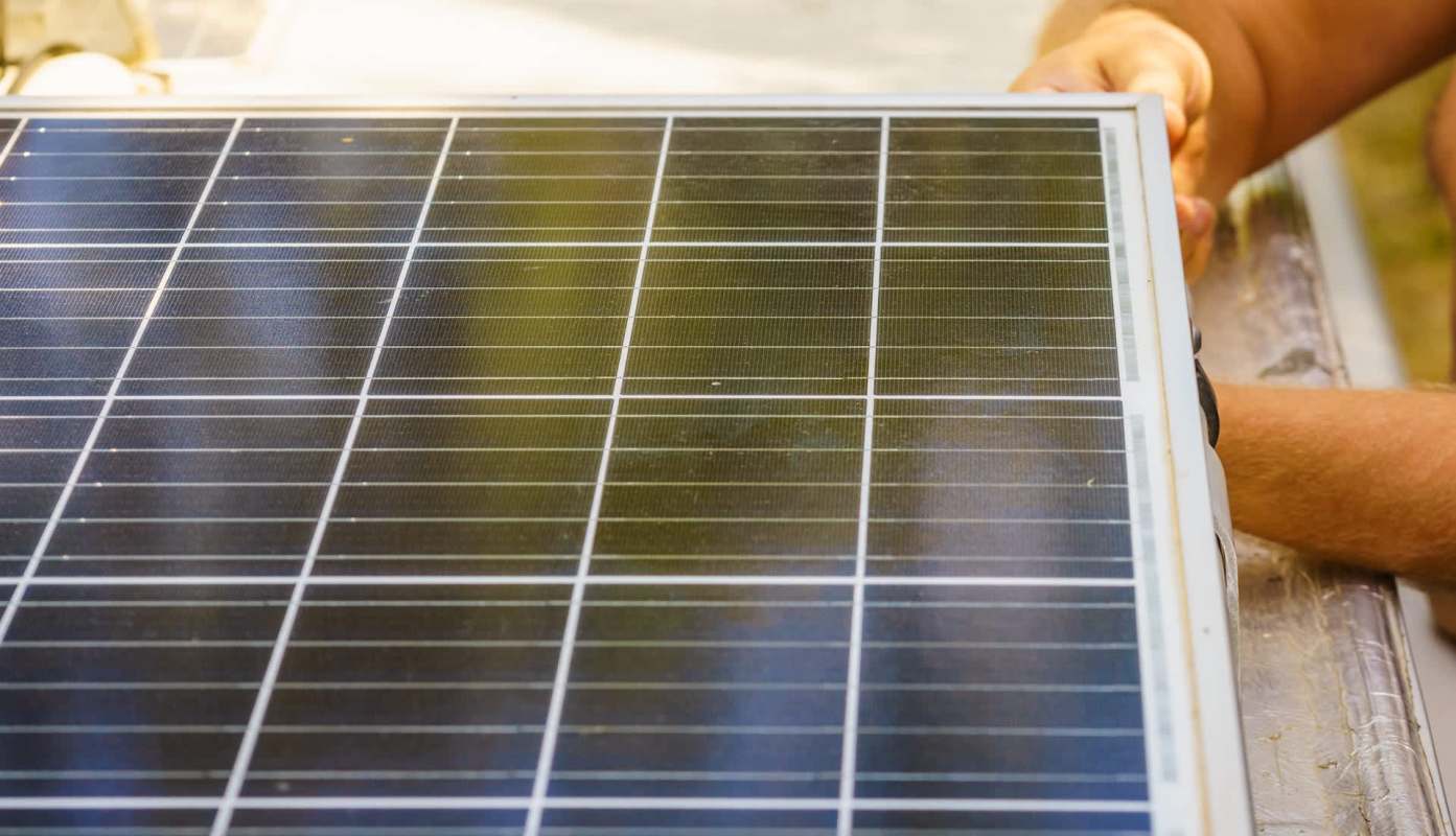 A person's hands hold a solar panel with visible cells and grid lines.