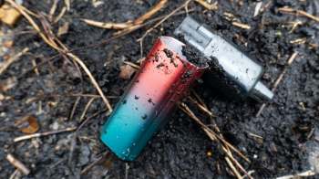 A colorful vape device partially buried in dark soil.
