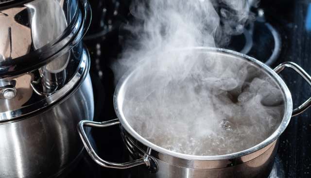 A pot of boiling water emits steam on a stovetop.