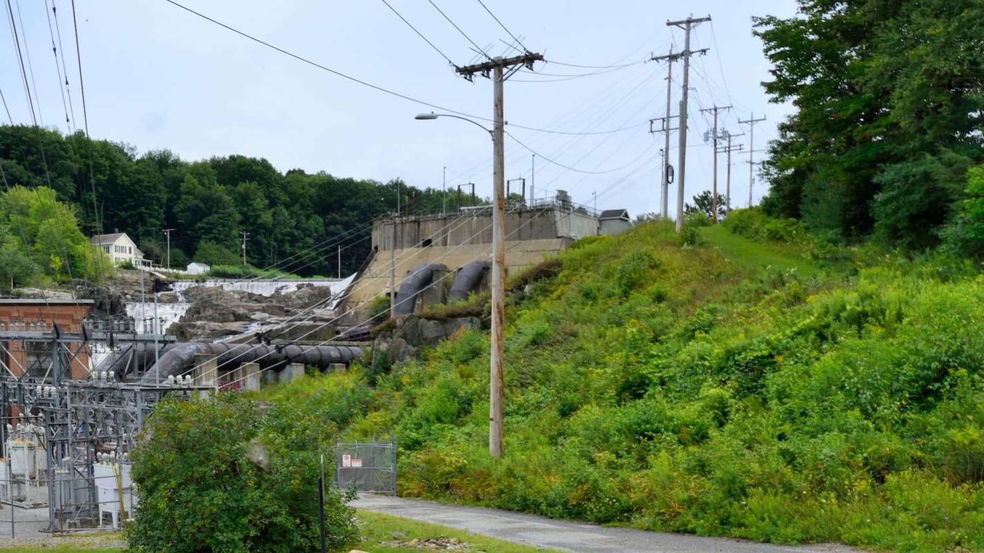 A hydroelectric facility with power lines and a small waterfall surrounded by greenery.