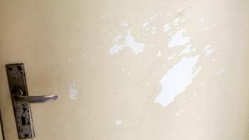 A close-up of a weathered door surface with peeling paint and a metallic handle.
