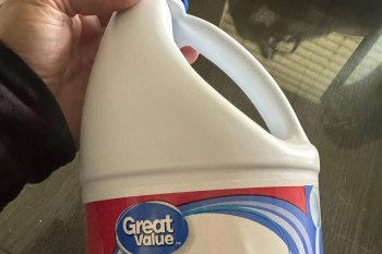 A hand holding a plastic container of Great Value bleach.