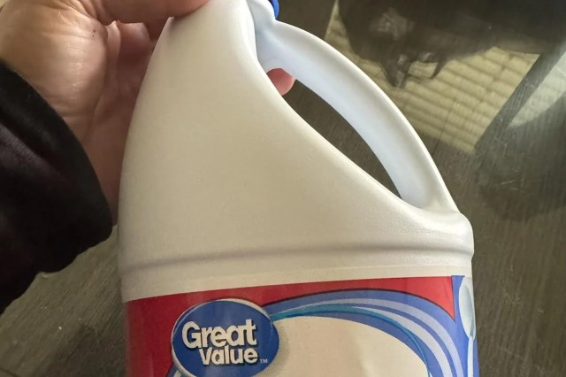 A hand holding a plastic container of Great Value bleach.