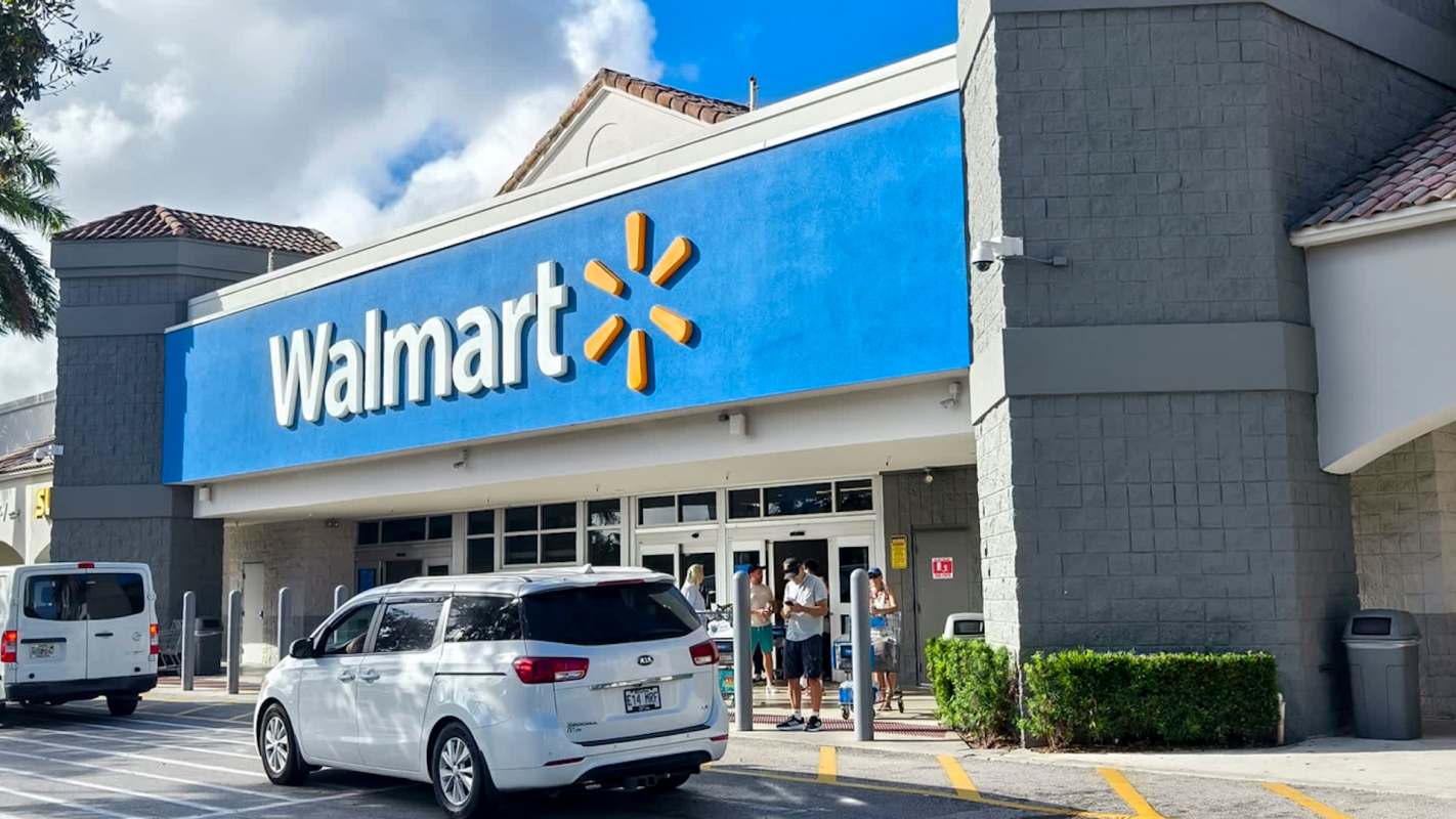 A Walmart store entrance with customers and vehicles parked outside.