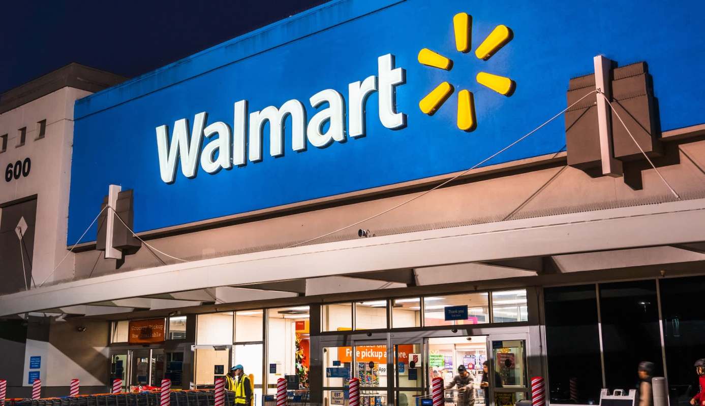 The exterior of a Walmart store at night with shoppers entering and exiting.
