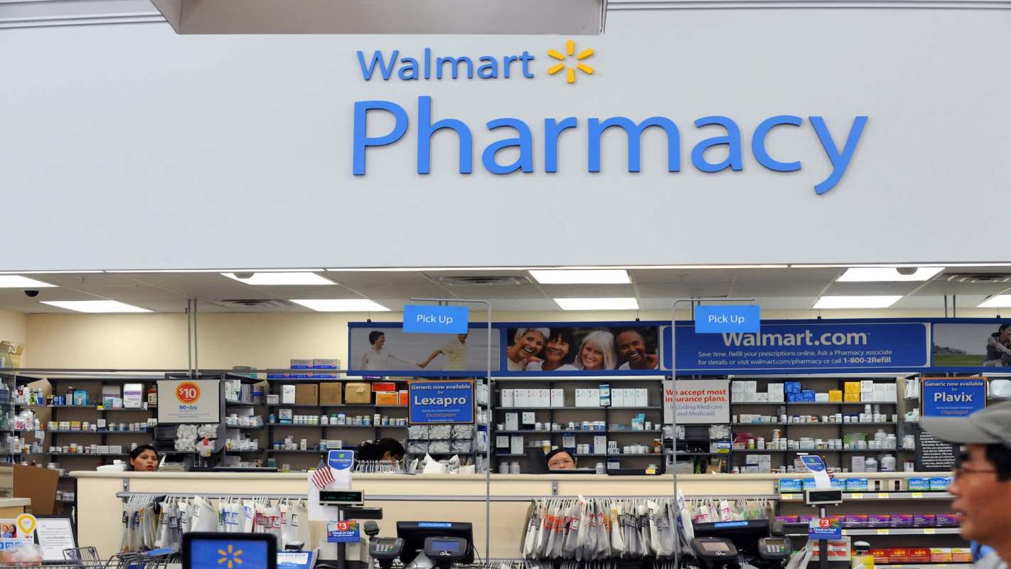 A Walmart pharmacy with shelves of medications and a sign indicating prescription pickup.