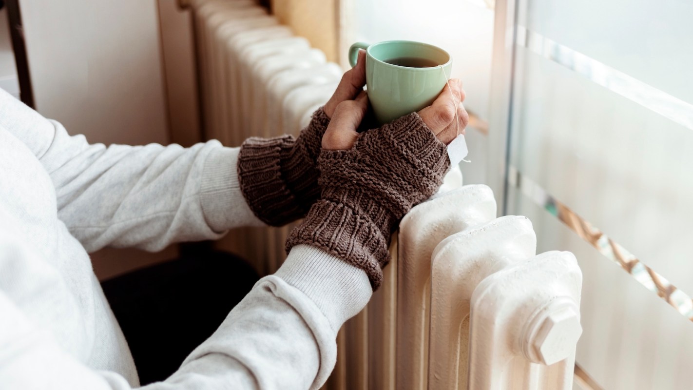 A person holding a green mug of tea while sitting beside a radiator.