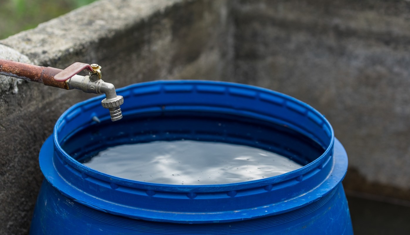 A metal faucet above a blue barrel filled with water.