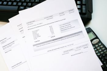 A utility bill document with a summary of charges and due date, placed on a desk next to a calculator and keyboard.