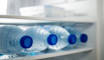 A row of plastic water bottles with blue caps in a refrigerator.