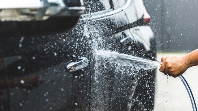 A person washing a black car with a hose, spraying water.