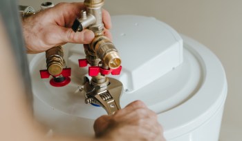 A person uses a wrench to tighten valves on a water heater.