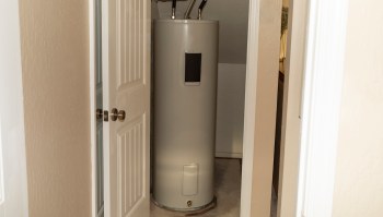 A water heater in a small, enclosed space with a door partially open.