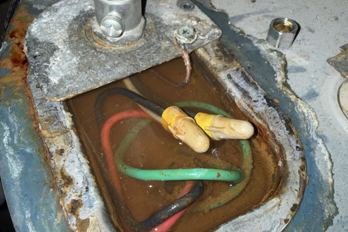 Electrical wires in a rusted compartment filled with brown water.