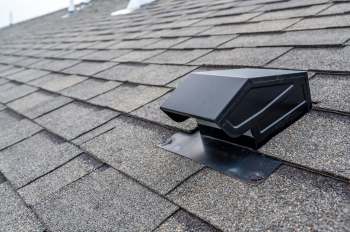 A black vent pipe on a textured asphalt shingle roof.