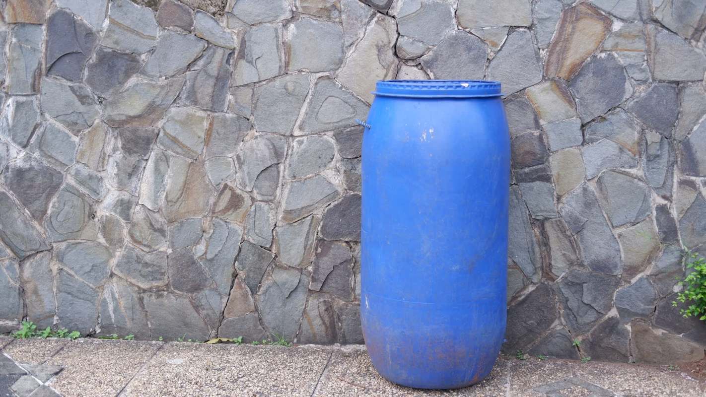 A blue plastic barrel beside a stone wall.