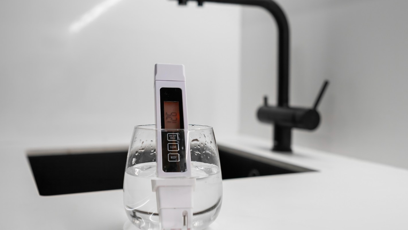 A digital temperature meter rests in a glass of water on a countertop.