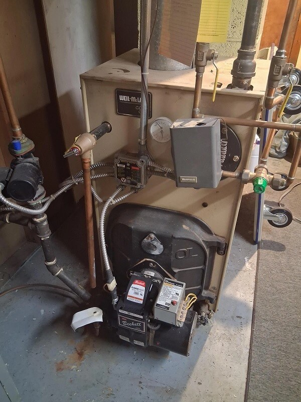 A heating system with valves, wires, and a control box in a basement setting.