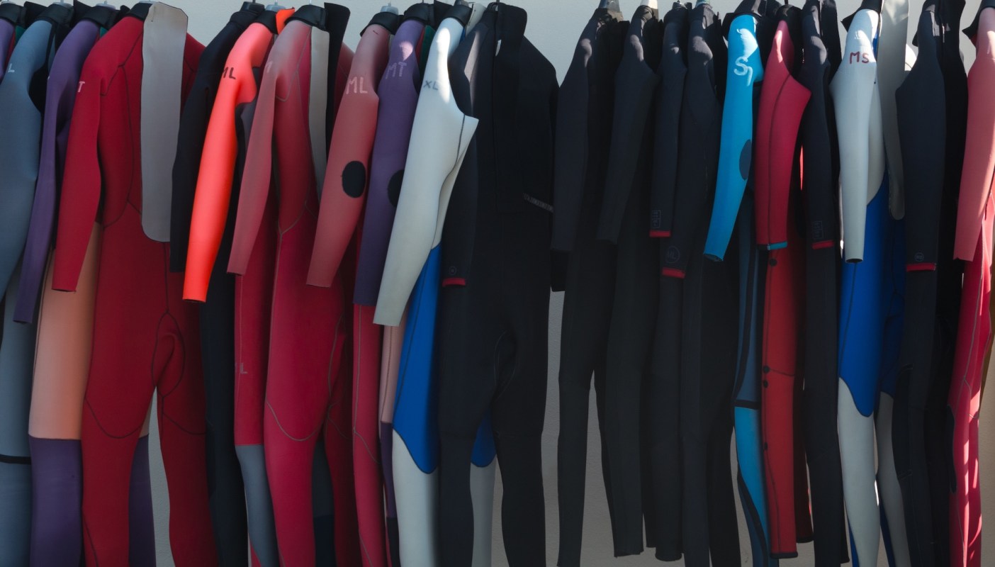 A variety of wetsuits hanging on display in different colors and sizes.