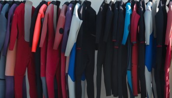 A variety of wetsuits hanging on display in different colors and sizes.