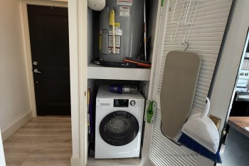 A water heater in a closet above a washing machine.