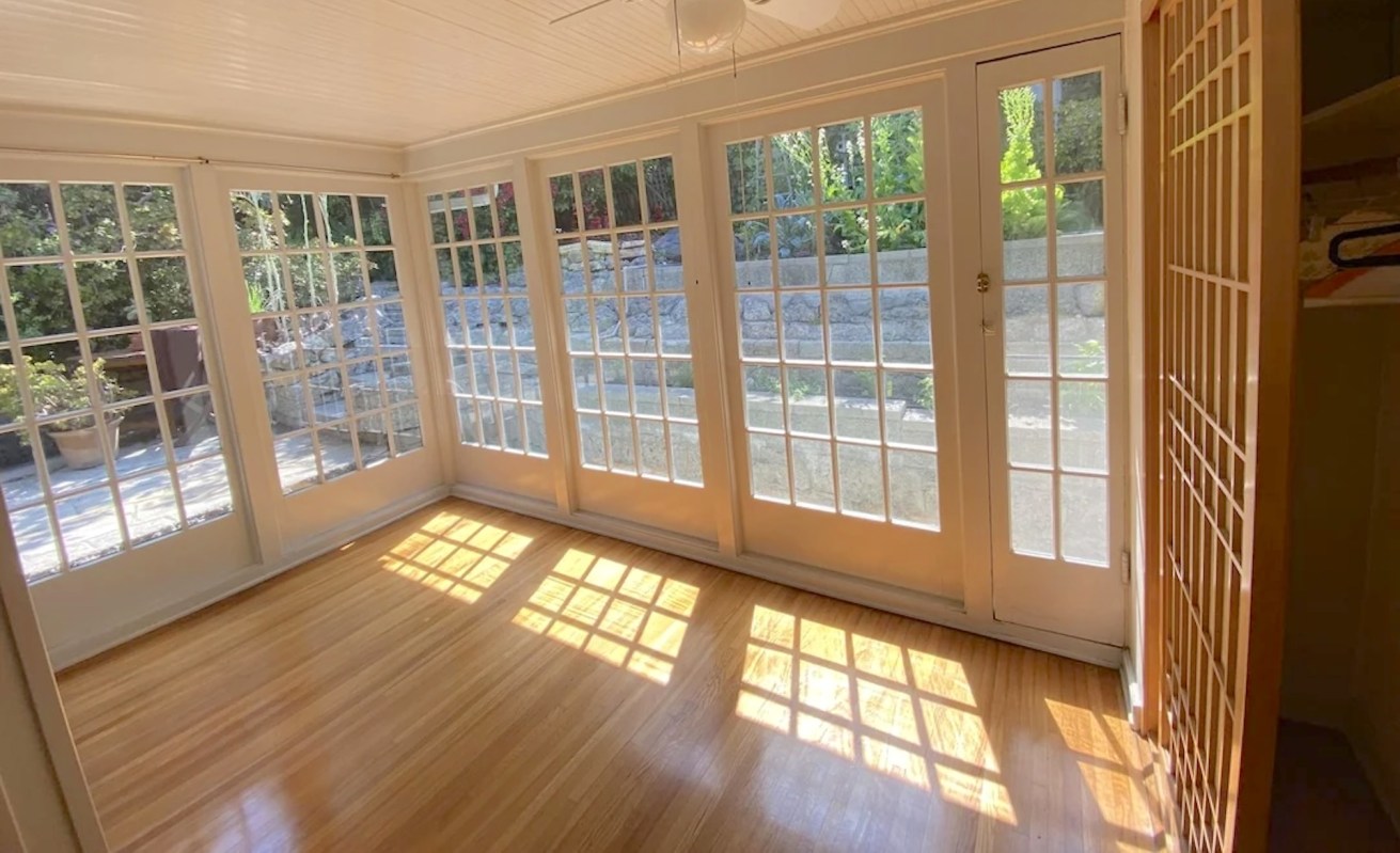 A sunroom with wood floors and single-pane windows.