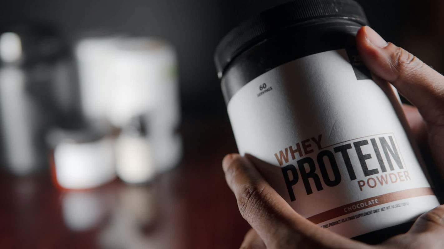 A hand holding a container of chocolate whey protein powder.