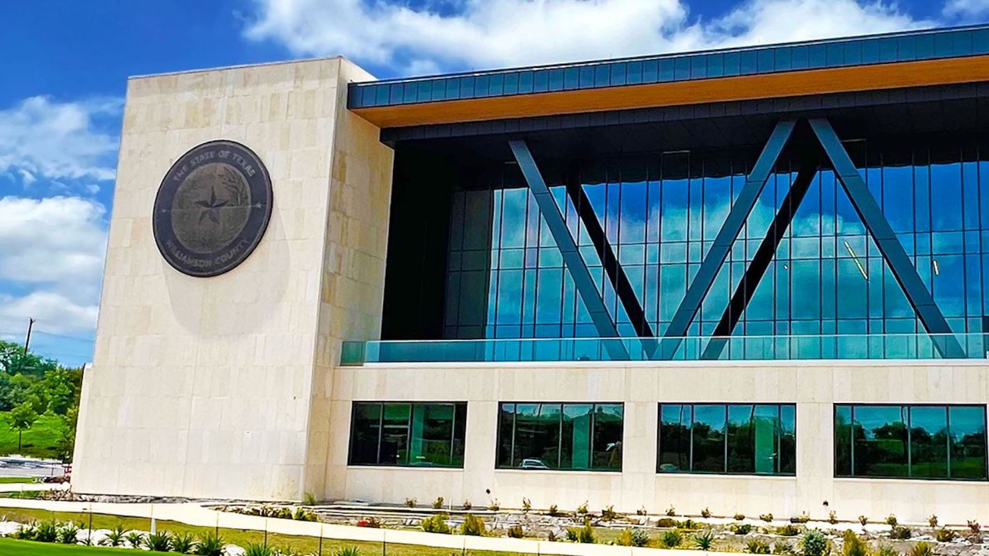 A modern building featuring large windows and a Texas state seal on the facade.