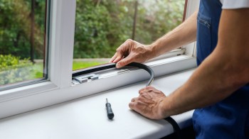 A person installs weather stripping on a window with a screwdriver nearby.