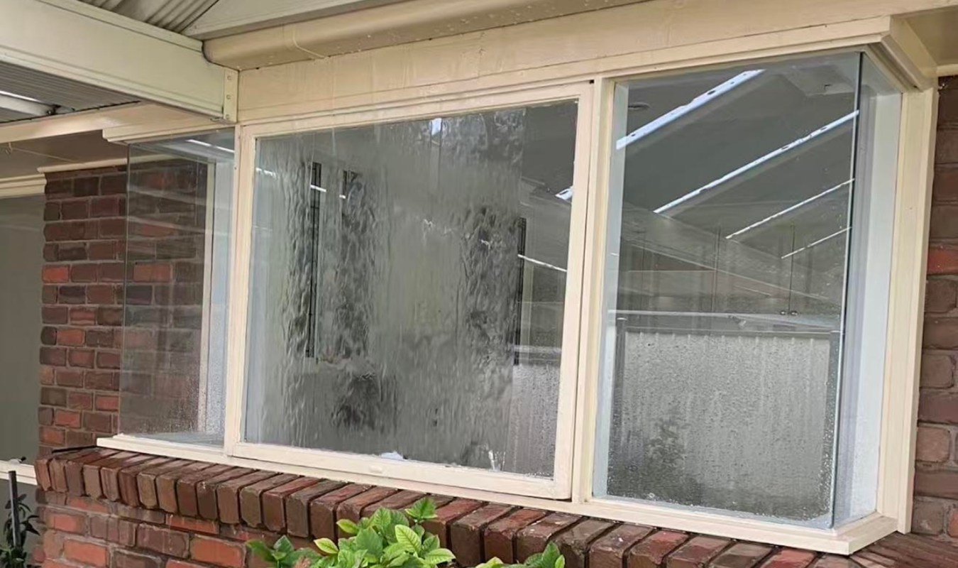 Water is cascading down a window, creating a misted effect on the glass near a brick wall.