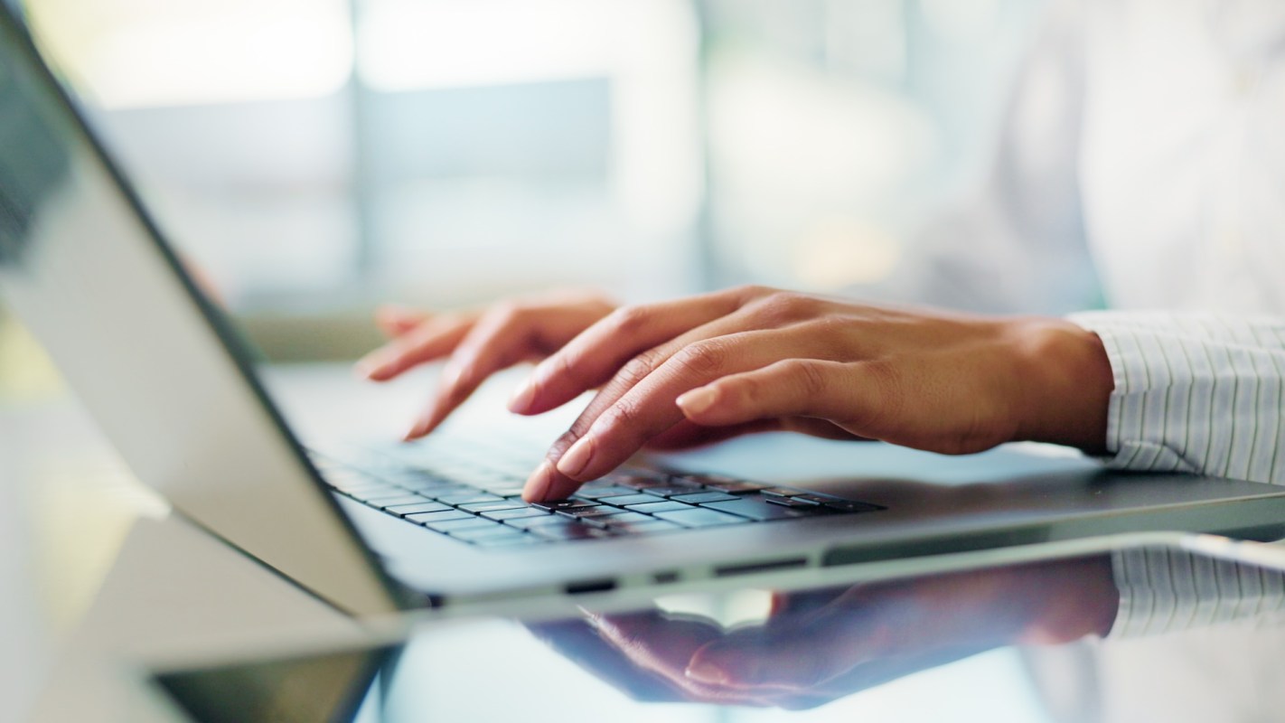 A person types on a laptop keyboard with a blurred background.
