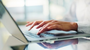 A person types on a laptop keyboard with a blurred background.