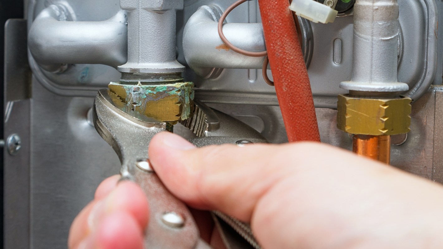 A hand using pliers to tighten a fitting on a metallic gas line.