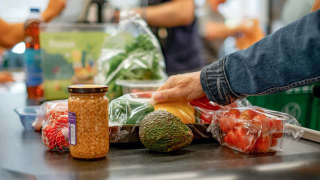 A hand reaches for colorful vegetables and a jar of lentils on a checkout counter.