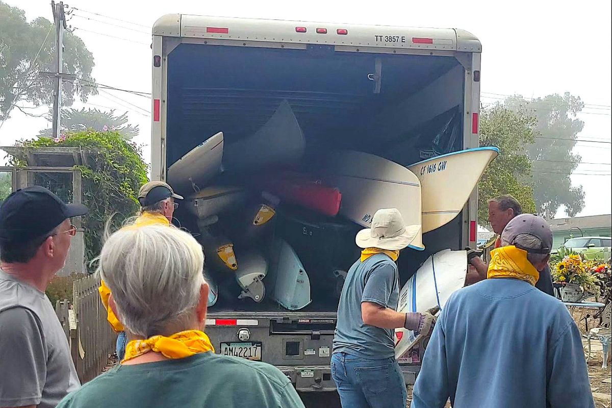 A group of people loading kayaks in the back of a moving truck.