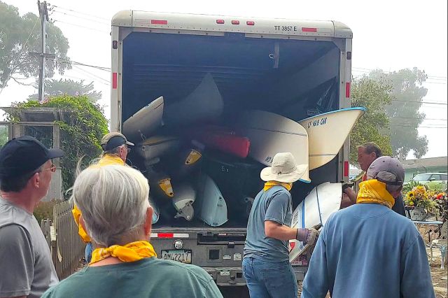 A group of people loading kayaks in the back of a moving truck.
