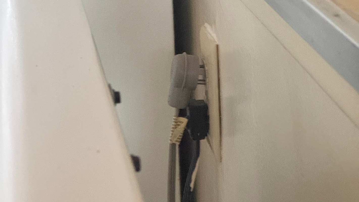 A power outlet with two cables plugged into it, partially obscured by furniture.